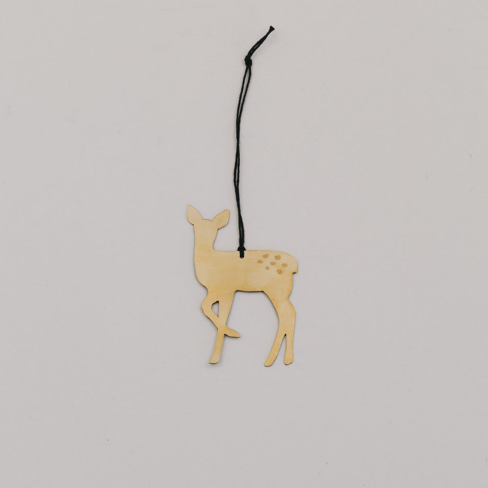 Goldener Rehnhänger aus Metall mit schwarzer Kordel auf hellem Hintergrund, minimalistisch arrangiert.