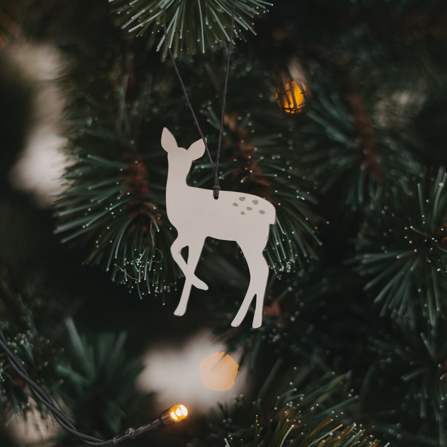 Glänzender silberner Rehanhänger am Weihnachtsbaum mit feinen Lichterketten im Hintergrund.
