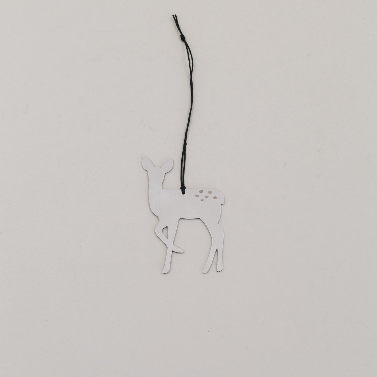 Silberner Rehnhänger aus Metall mit schwarzer Kordel auf hellem Hintergrund, minimalistisch arrangiert.