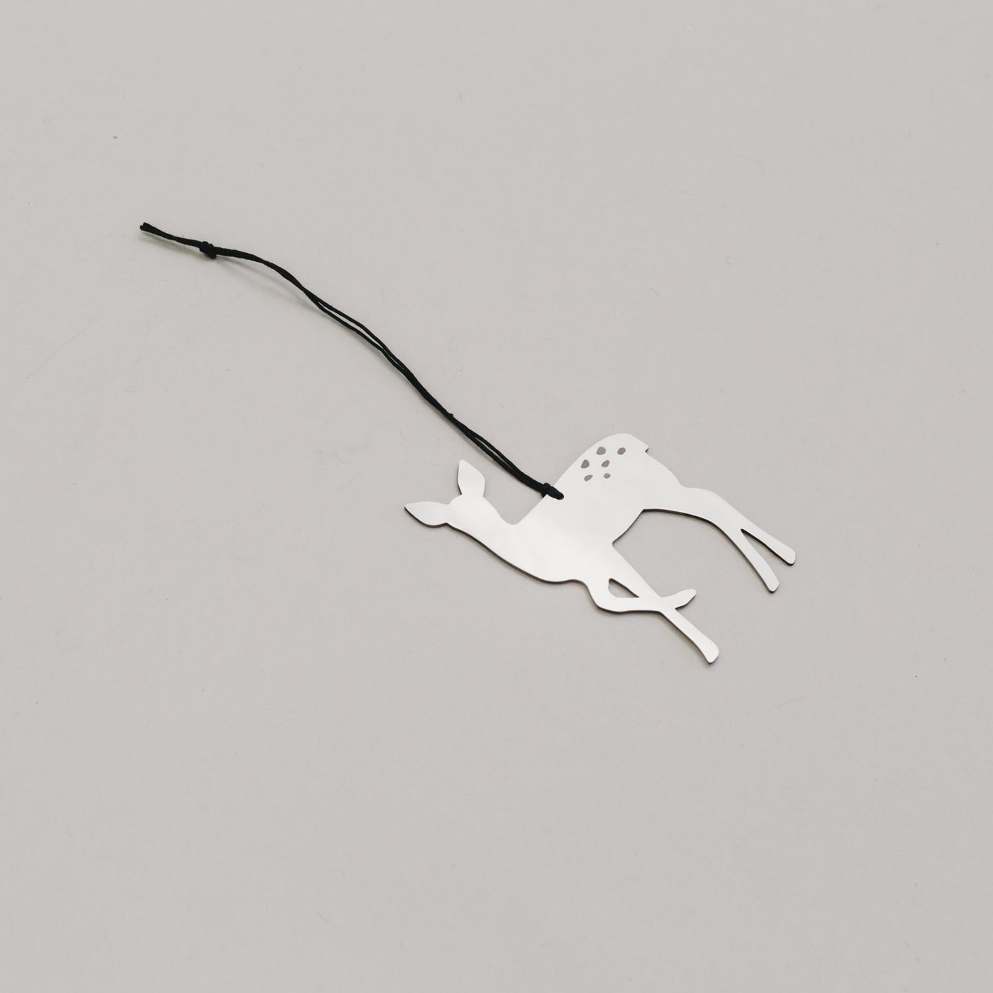 Schlichter silberner Rehanhänger aus Metall mit schwarzem Band, auf hellem Untergrund liegend. 