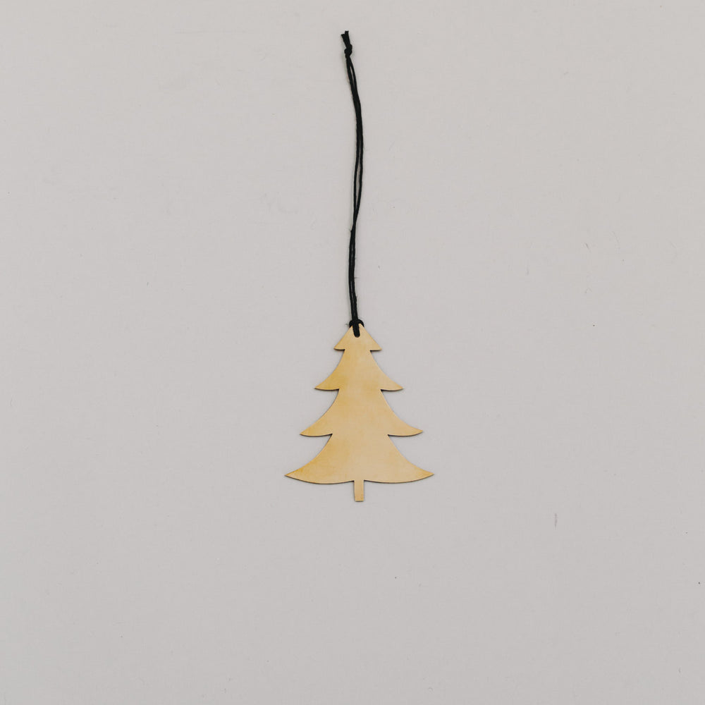 Goldener Tannenanhänger aus Metall mit schwarzer Kordel auf hellem Hintergrund, minimalistisch arrangiert.