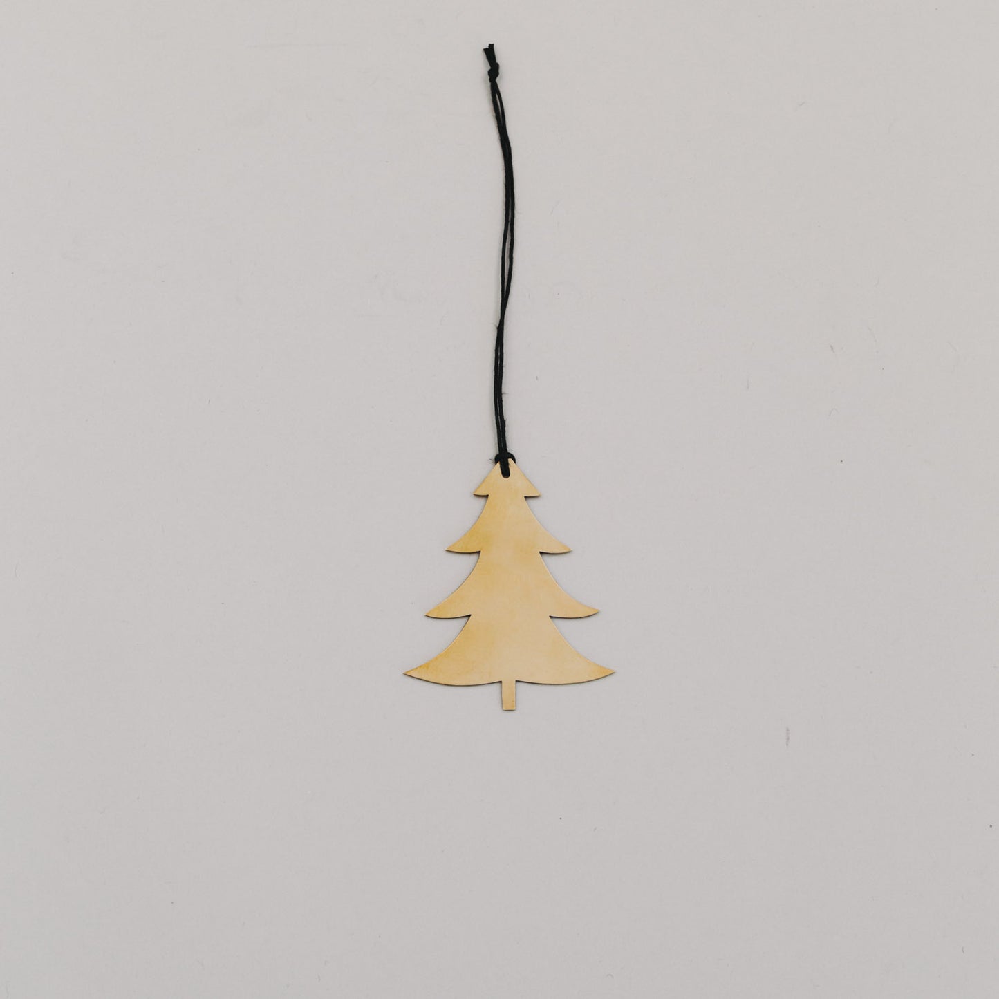 Goldener Tannenanhänger aus Metall mit schwarzer Kordel auf hellem Hintergrund, minimalistisch arrangiert.