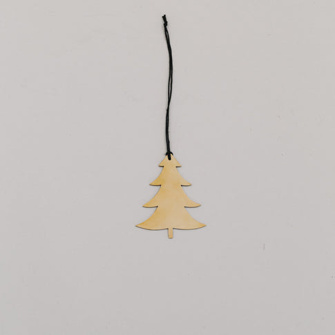 Goldener Tannenanhänger aus Metall mit schwarzer Kordel auf hellem Hintergrund, minimalistisch arrangiert.