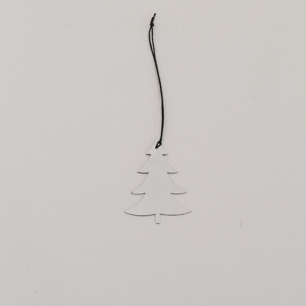 Silberner Tannenanhänger aus Metall mit schwarzer Kordel auf hellem Hintergrund, minimalistisch arrangiert.