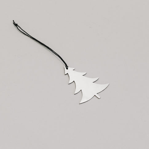 Schlichter silberner Tannenanhänger aus Metall mit schwarzem Band, auf hellem Untergrund liegend.