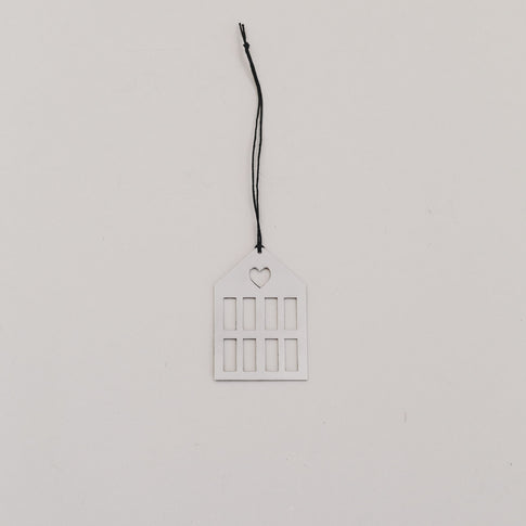 Silberner Hausanhänger aus Metall mit schwarzer Kordel auf hellem Hintergrund, minimalistisch arrangiert.