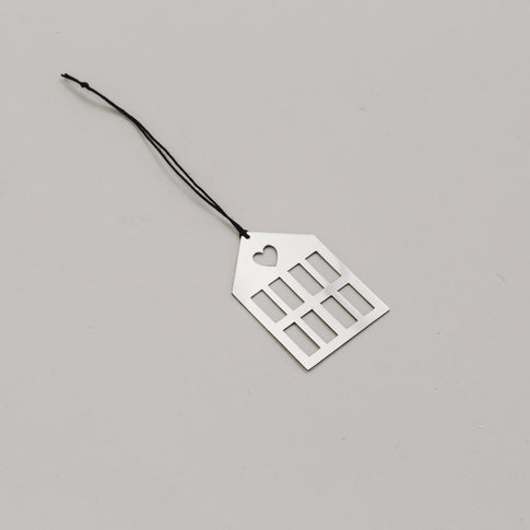 Schlichtersilberner Hausanhänger aus Metall mit schwarzem Band, auf hellem Untergrund liegend.