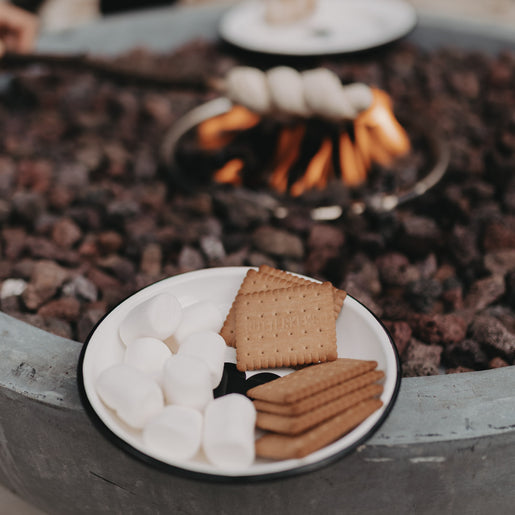 Emaille Teller Herz mit Butterkeksen und Marshmallows vor einem Lagerfeuer – gemütliches Outdoor-Feeling.