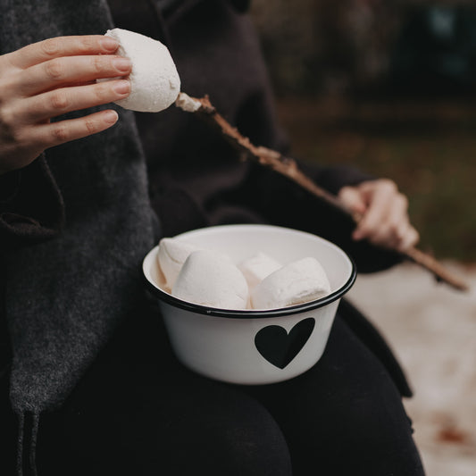 Person hält Emaille Schale Herz mit Marshmallows – perfekt für gemütliche Momente am Lagerfeuer.