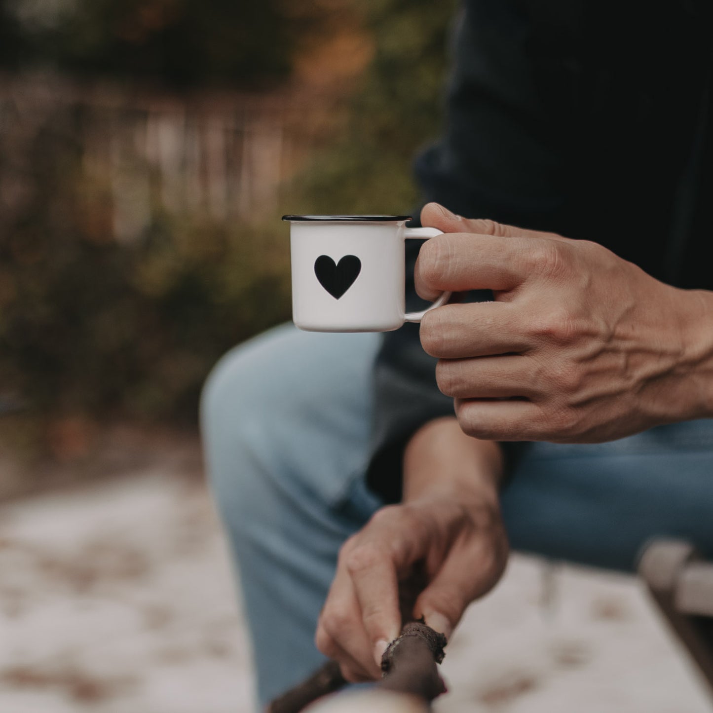Hand hält Emaille Espressotasse Herz am Lagerfeuer – stilvoller Begleiter für Espresso im Freien.