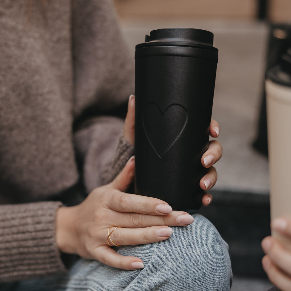 Nahaufnahme To-go Becher Herz schwarz in der Hand gehalten, stilvoller Becher für unterwegs.