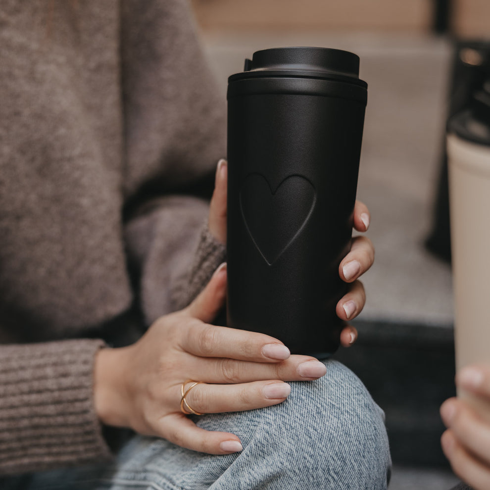 Nahaufnahme To-go Becher Herz schwarz in der Hand gehalten, stilvoller Becher für unterwegs.