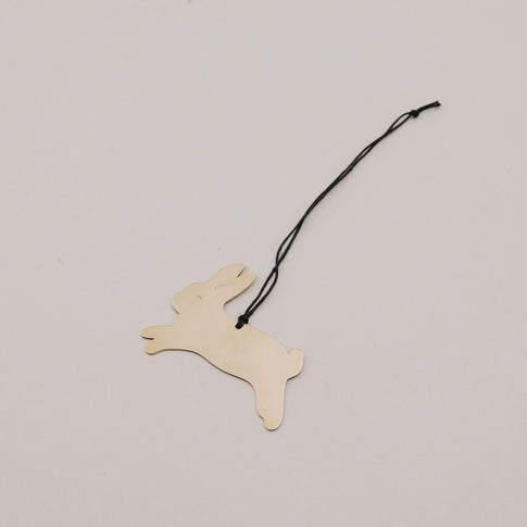 Einzelner goldener Metallanhänger Hase springend auf hellem Untergrund.