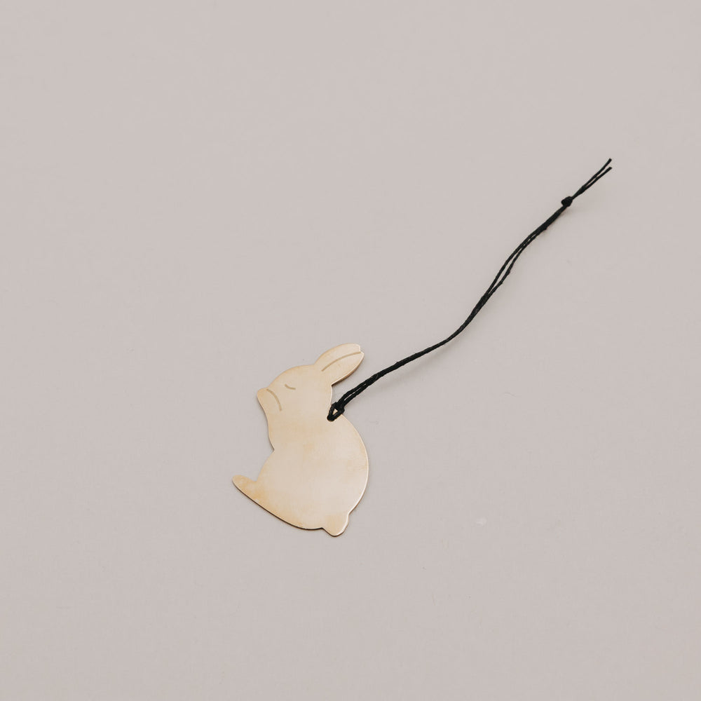 Einzelner goldener Metallanhänger sitzender Hase mit Band auf hellem Hintergrund.