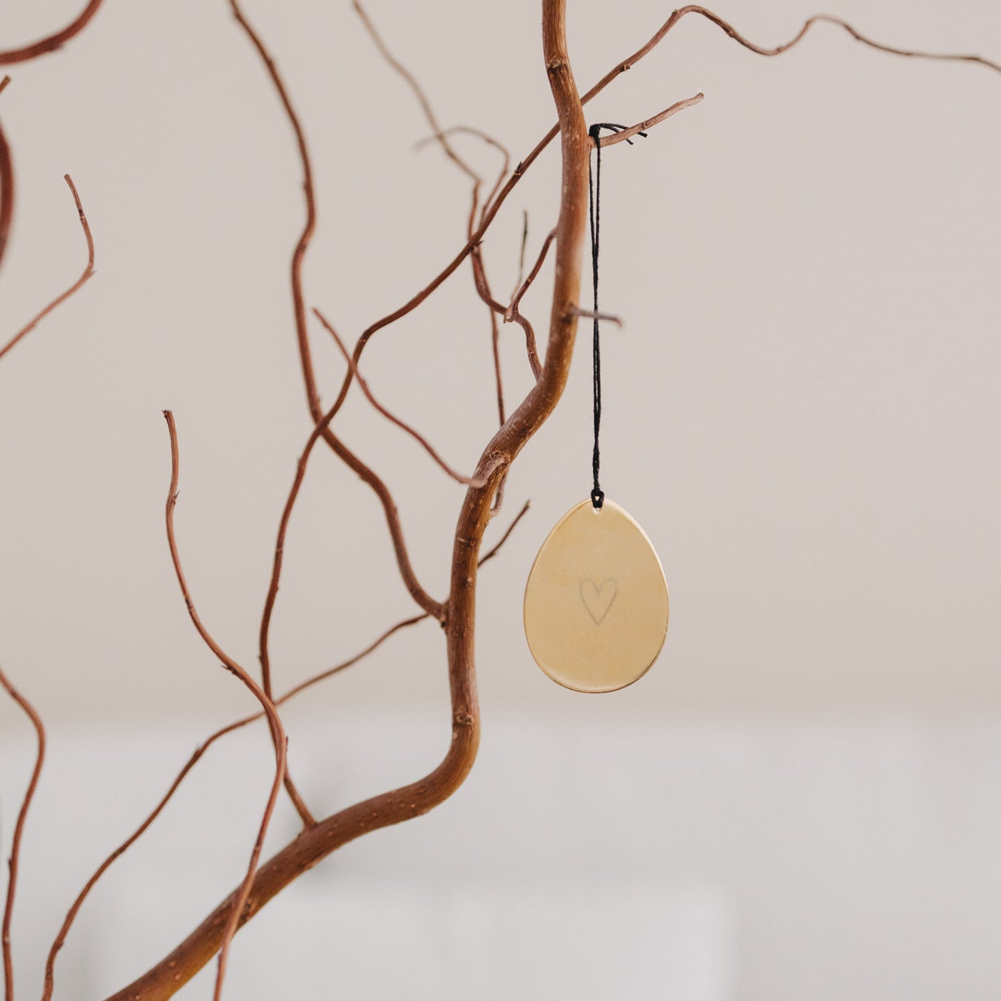 Goldener Metallanhänger Ei mit Herzgravur am Dekoast aufgehängt.