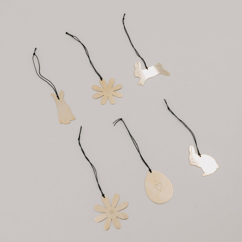 Goldene Metallanhänger Blume, Ei und Hasen auf hellem Hintergrund arrangiert.