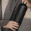 Detailaufnahme einer mattschwarzen Trinkflasche mit geprägtem Herzmotiv und silbernem Flaschenhals in einer Hand.