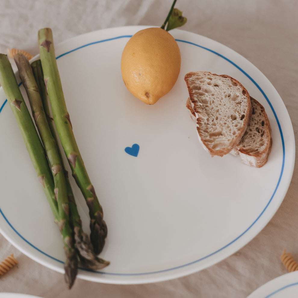 Runder Porzellanteller mit hellblauem Rand und Herzdetail, belegt mit Spargel, Zitrone und Brot.