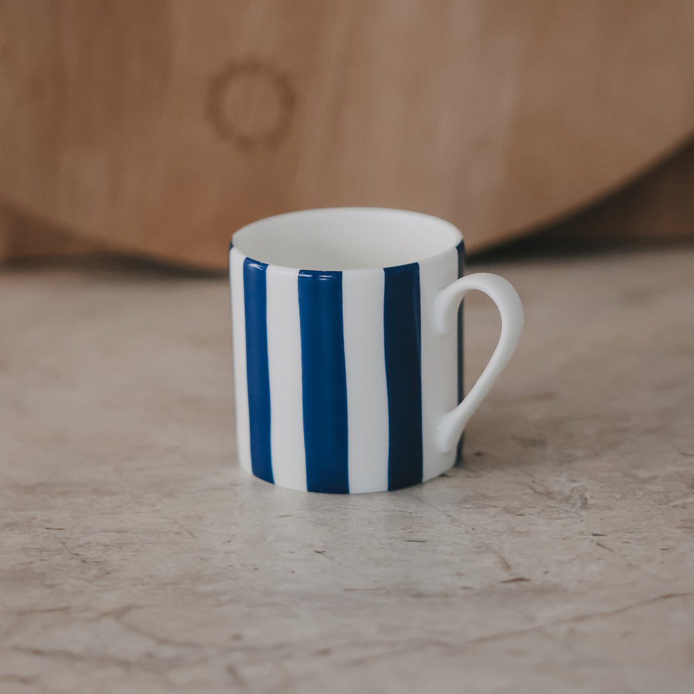 Einzelne Tasse mit dunkelblauen, vertikalen Streifen vor ruhigem, neutralem Hintergrund.