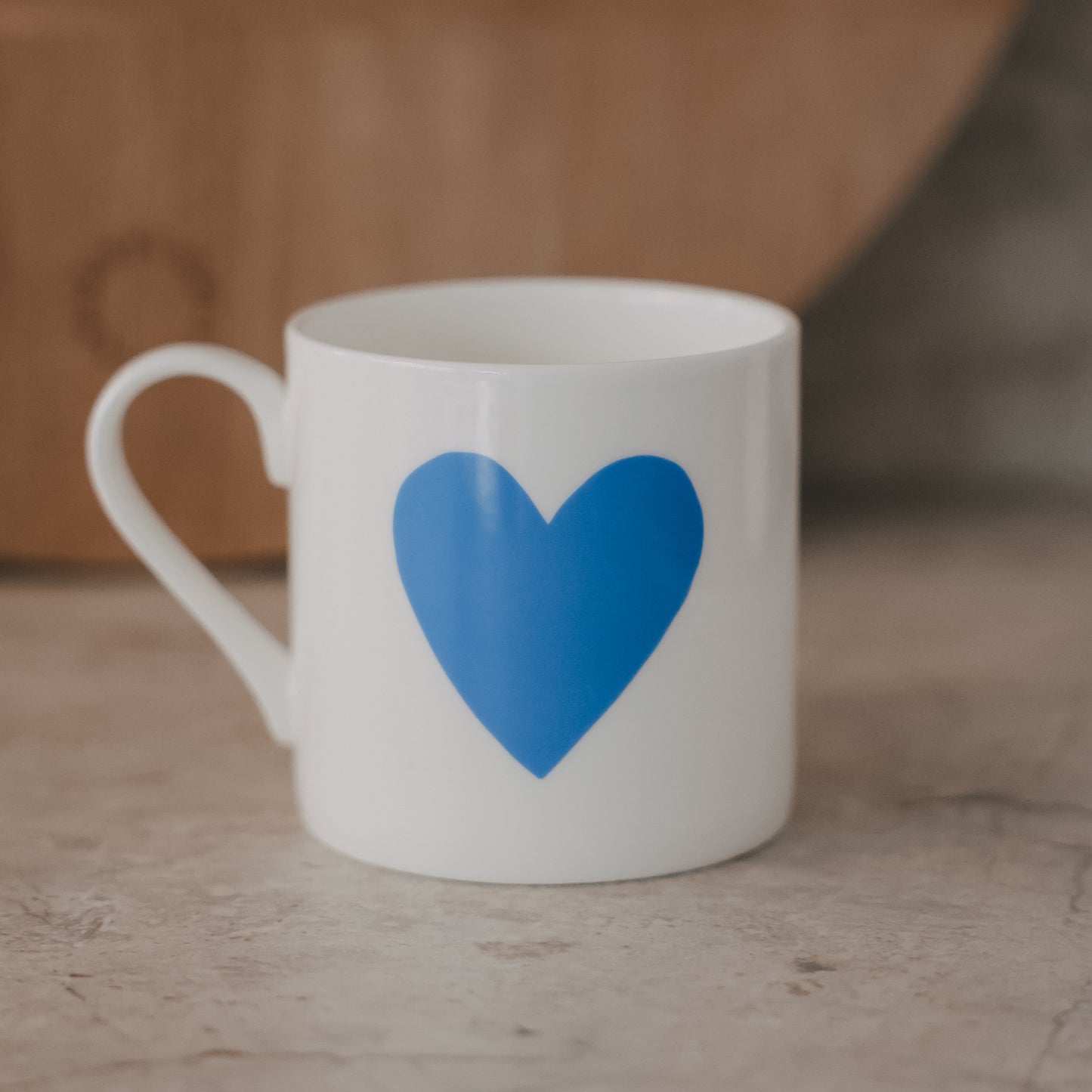 Weiße Tasse mit großem hellblauen Herz auf der Vorderseite vor warmem Hintergrund