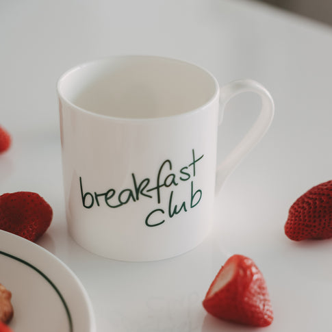 Frühstücksszene mit weißer Tasse mit grünem Schriftzug und Erdbeeren auf hellem Hintergrund