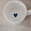 Weiße Tasse mit dunkelblauem Herz auf der Innenseite, Draufsicht auf hellem Untergrund