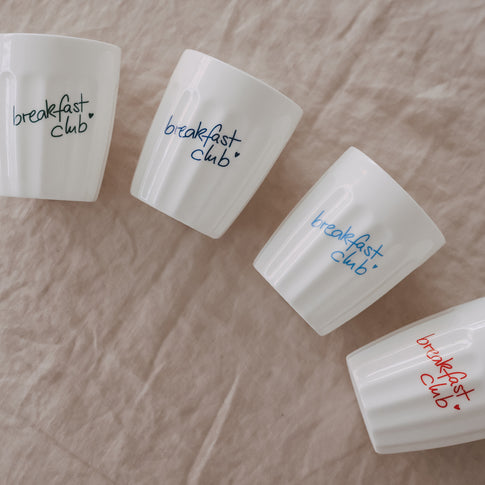 Keramikbecher „breakfast club“ in Blau und Grün dekorativ auf hellem Stoff angerichtet