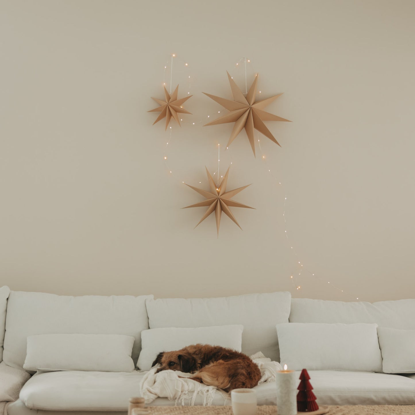 Drei braune Papiersterne mit Lichterkette als natürliche Weihnachtsdeko über einem weißen Sofa