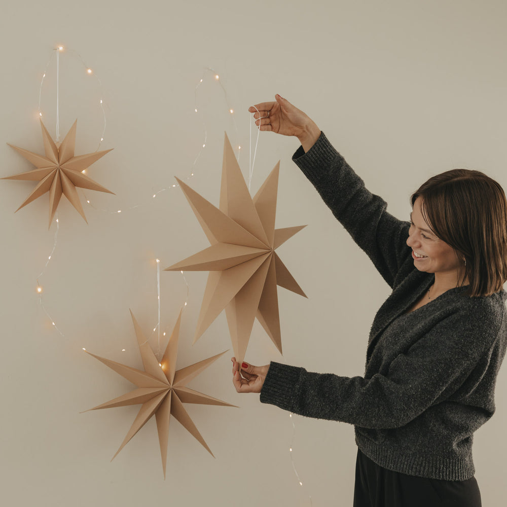 Braune Papiersterne mit Lichterkette, großer Stern wird dekorativ in der Hand gehalten