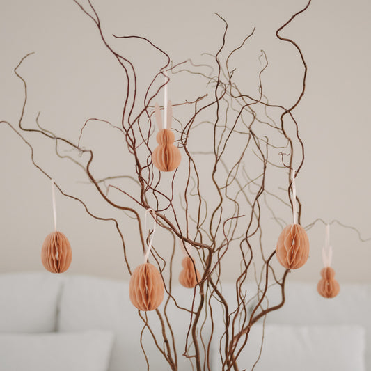 Peachfarbene Papieranhänger in Ei- und Hasenform hängen an dekorativen Zweigen.