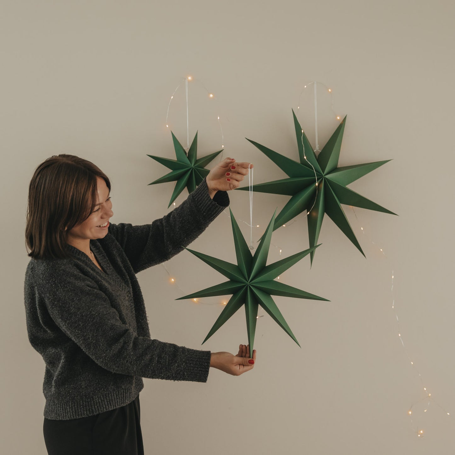 Drei dunkelgrüne Papiersterne mit Lichterkette, einer davon wird dekorativ in der Hand gehalten
