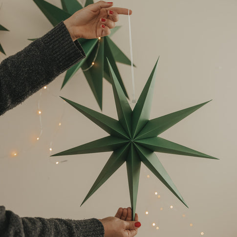 Dunkelgrüner Papierstern mit langen Spitzen und weißer Aufhängung als moderne Weihnachtsdekoration