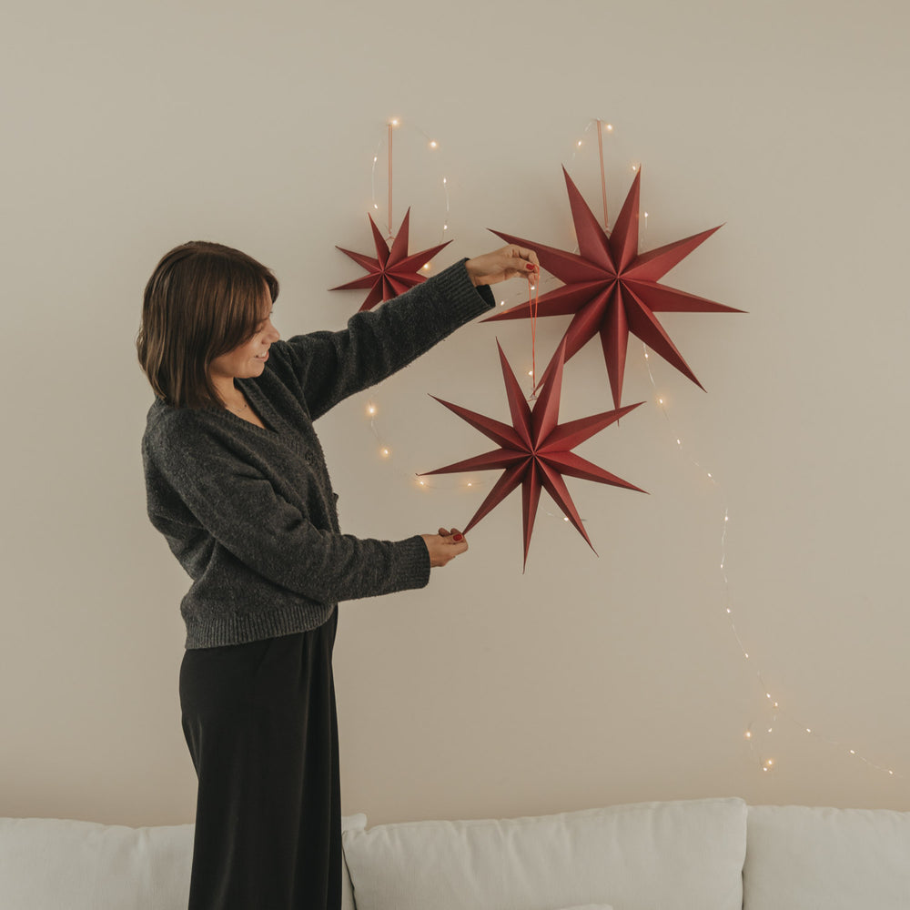 Drei rote Papiersterne in verschiedenen Größen mit warmer Lichterkette als festliche Weihnachtsdekoration