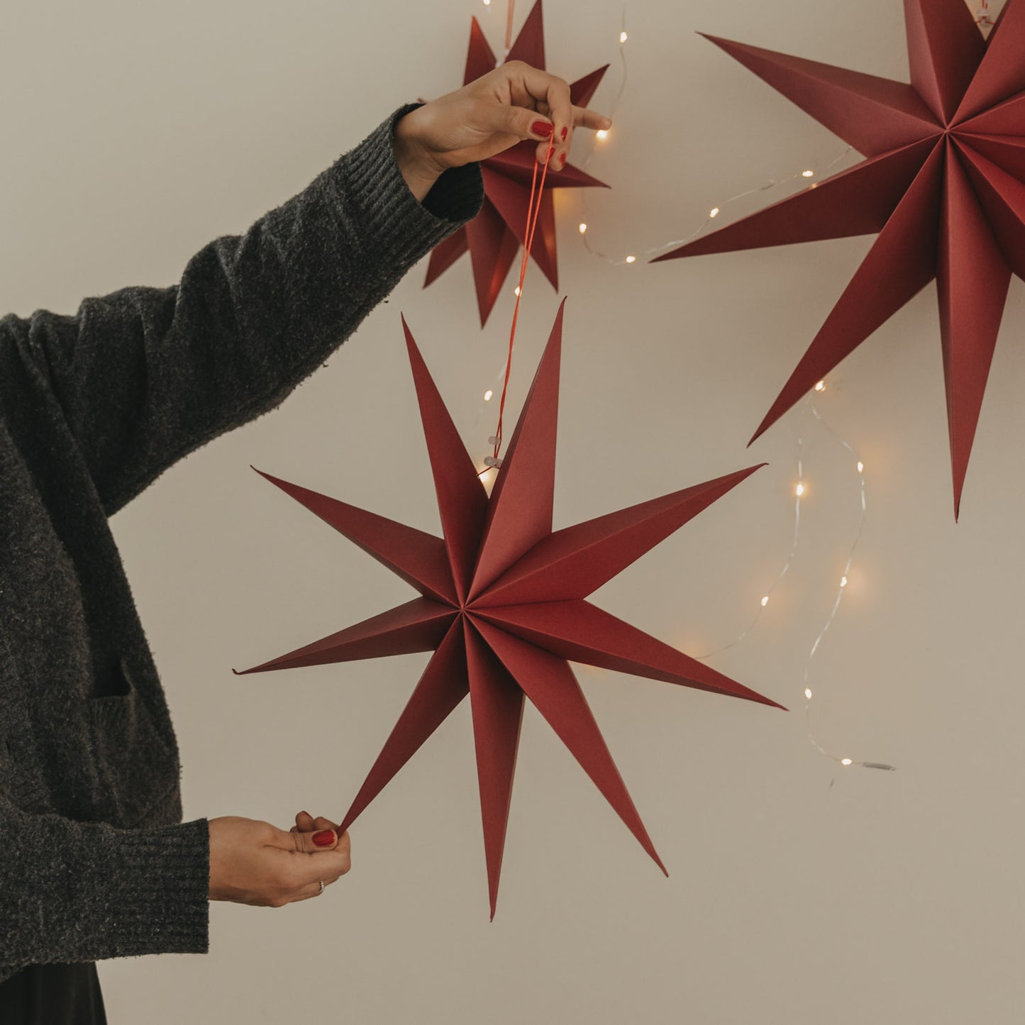 Roter Papierstern mit langen Spitzen und Aufhängung vor einer warm leuchtenden Lichterkette
