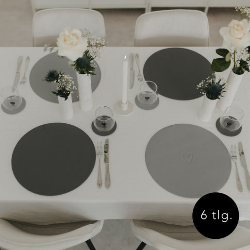 Gesamtansicht eines gedeckten Tisches mit grauen Platzsets und weißen Blumenvasen.