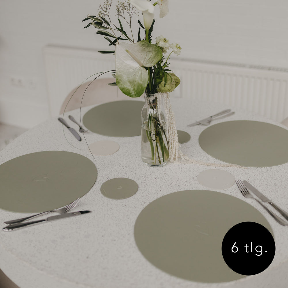 Gedeckter Tisch mit grünen Platzsets und passenden Untersetzern in Grün.