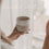 Ein handgetöpferter Becher mit der Prägung "Guten Morgen" ist in der Hand einer jugen Frau, die aus dem Fenster schaut.