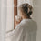 Eine junge Frau mit einer locker gebunden Zopf schaut verträumt aus dem Fenster und hält dabei einen Becher mit der Prägung "Guten Morgen" in ihrer Hand.