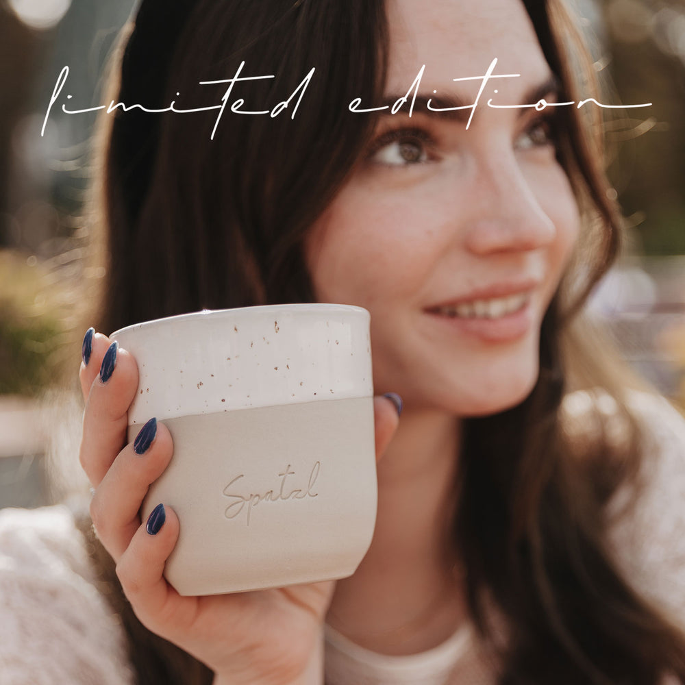 Junge Frau mit langem Haar lächelt und hält den Becher „Spatzl“ in die Kamera.