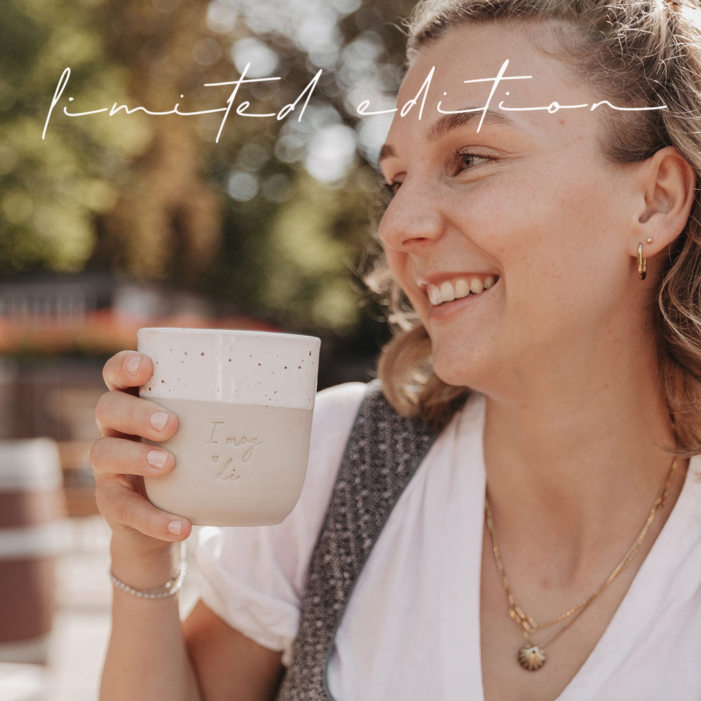 Frau im Dirndl hält den Becher mit der Gravur „I mog di“ und lächelt glücklich in die Kamera.