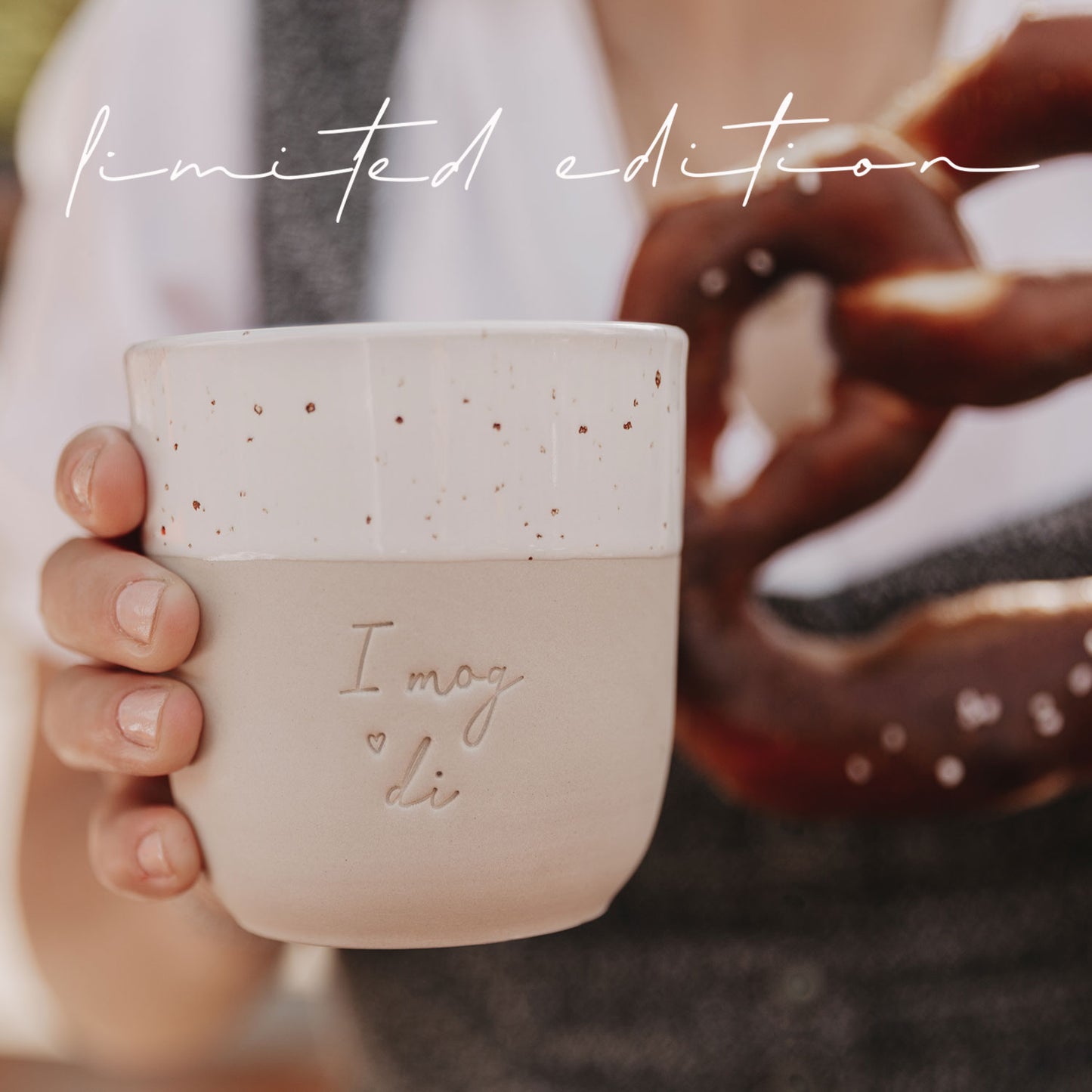 Detailaufnahme des Bechers „I mog di“ mit Brezel im Hintergrund auf einem Holztisch.