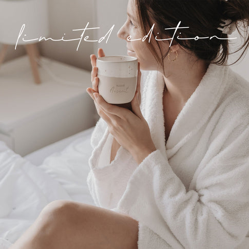 Frau im Bademantel hält Keramikbecher „Kleine Auszeit“ in ruhiger Morgenstimmung – Limited Edition.