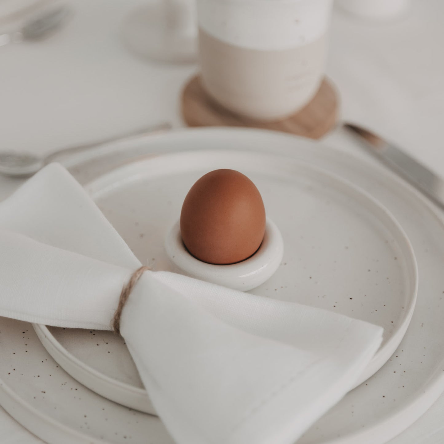 Braunes Ei im Calma Eierbecher auf gedecktem Tisch mit Leinenserviette und Teller in natürlichem Look
