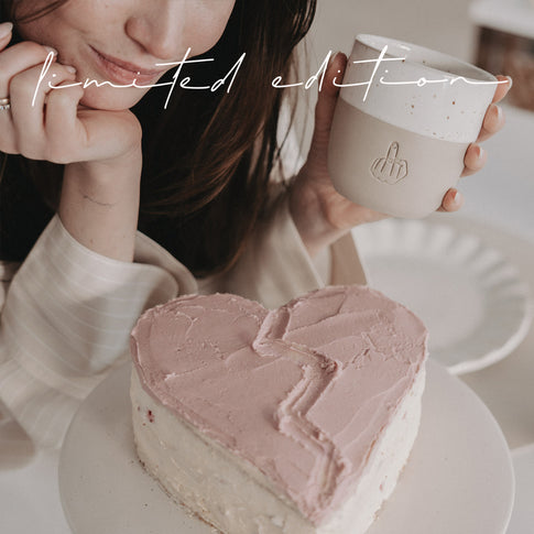 Limitierter Becher „Nein Danke“ mit Mittelfinger-Motiv, Person hält Becher neben herzförmigem Kuchen, Valentinstag Edition.