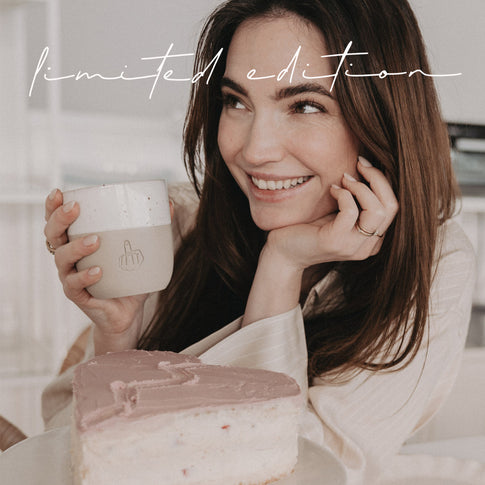 Frau mit Limited Edition Keramikbecher sitzt vor einem herzförmigen Kuchen und lächelt.