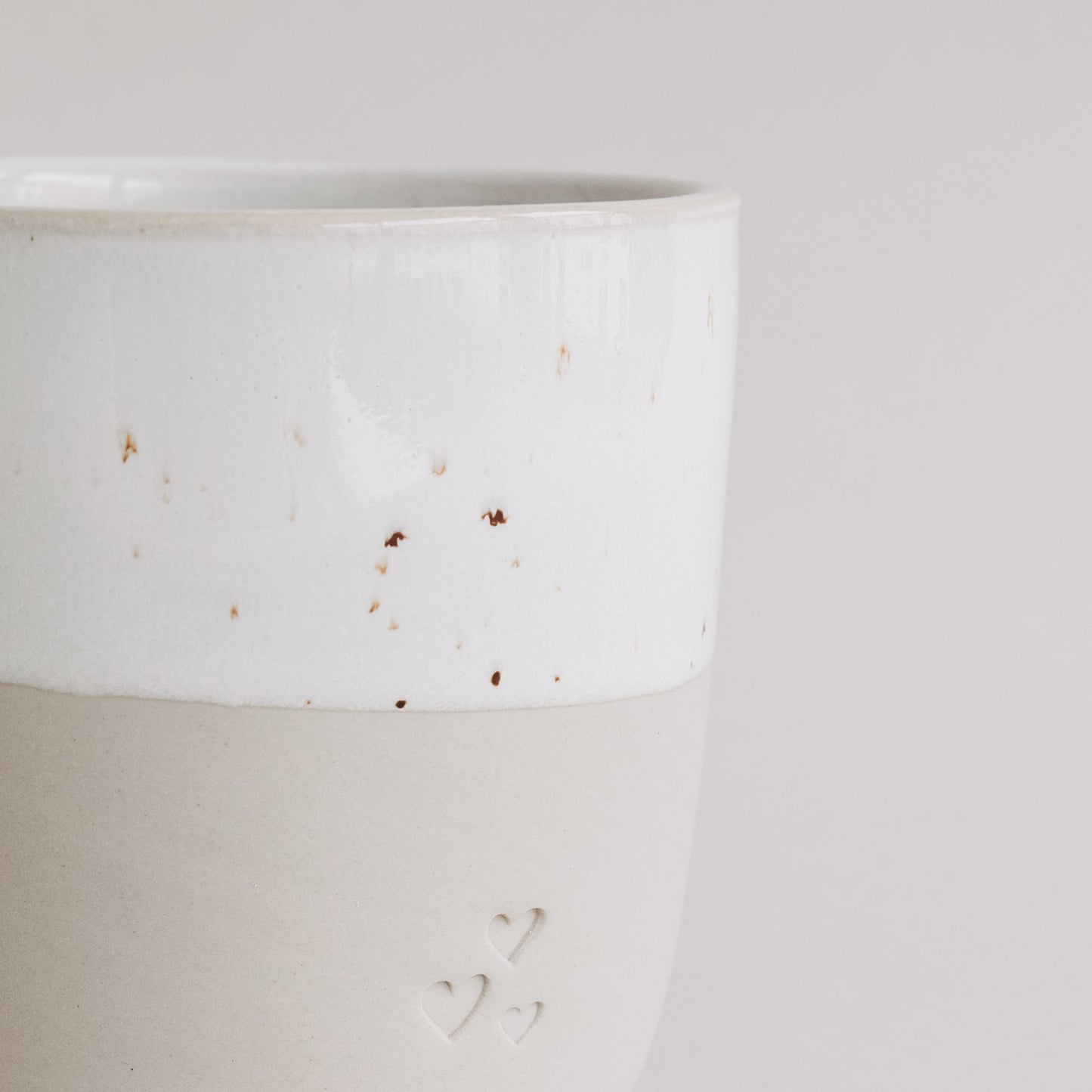 Detailaufnahme des zweifarbigen Keramikbechers mit Herzprägung und gesprenkelter weißer Glasur.