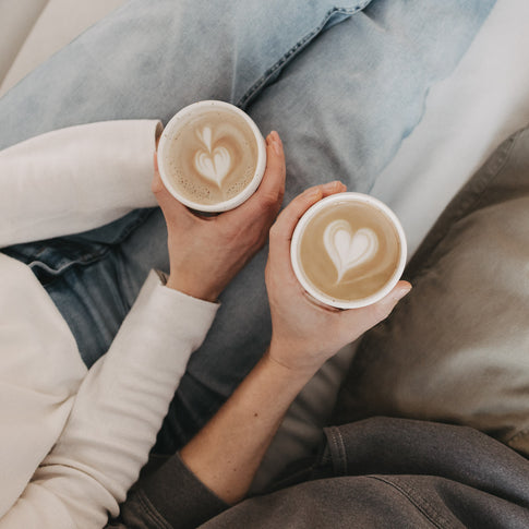 Zwei Cappuccinos in MRS und MR Bechern mit Herz-Latte-Art von oben.