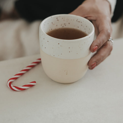 Keramikbecher mit Zuckerstangen-Motiv, gefüllt mit Tee, daneben Zuckerstange, minimalistisch und winterlich