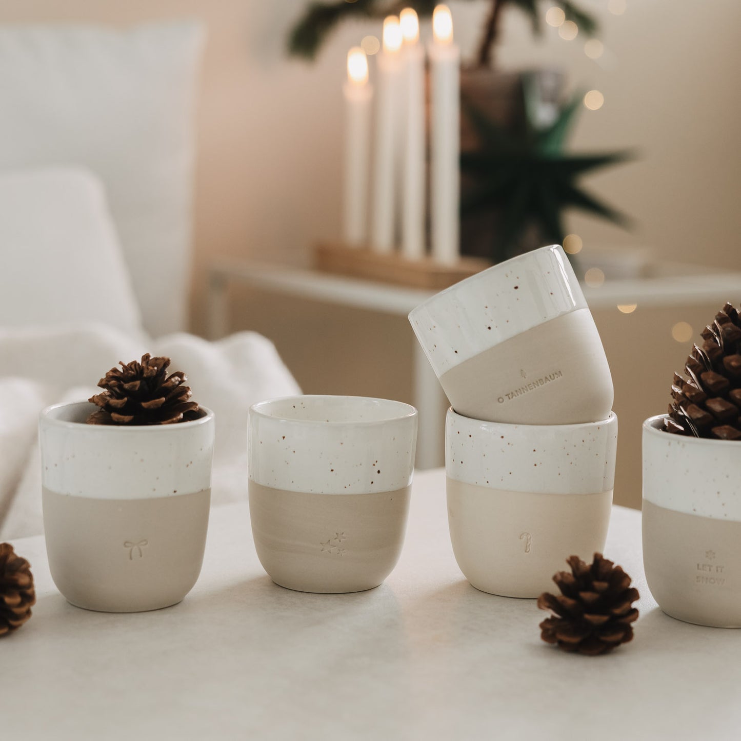 Set Keramikbecher mit Weihnachtsmotiven, dekoriert mit Tannenzapfen, stilvolle winterliche Tischdekoration