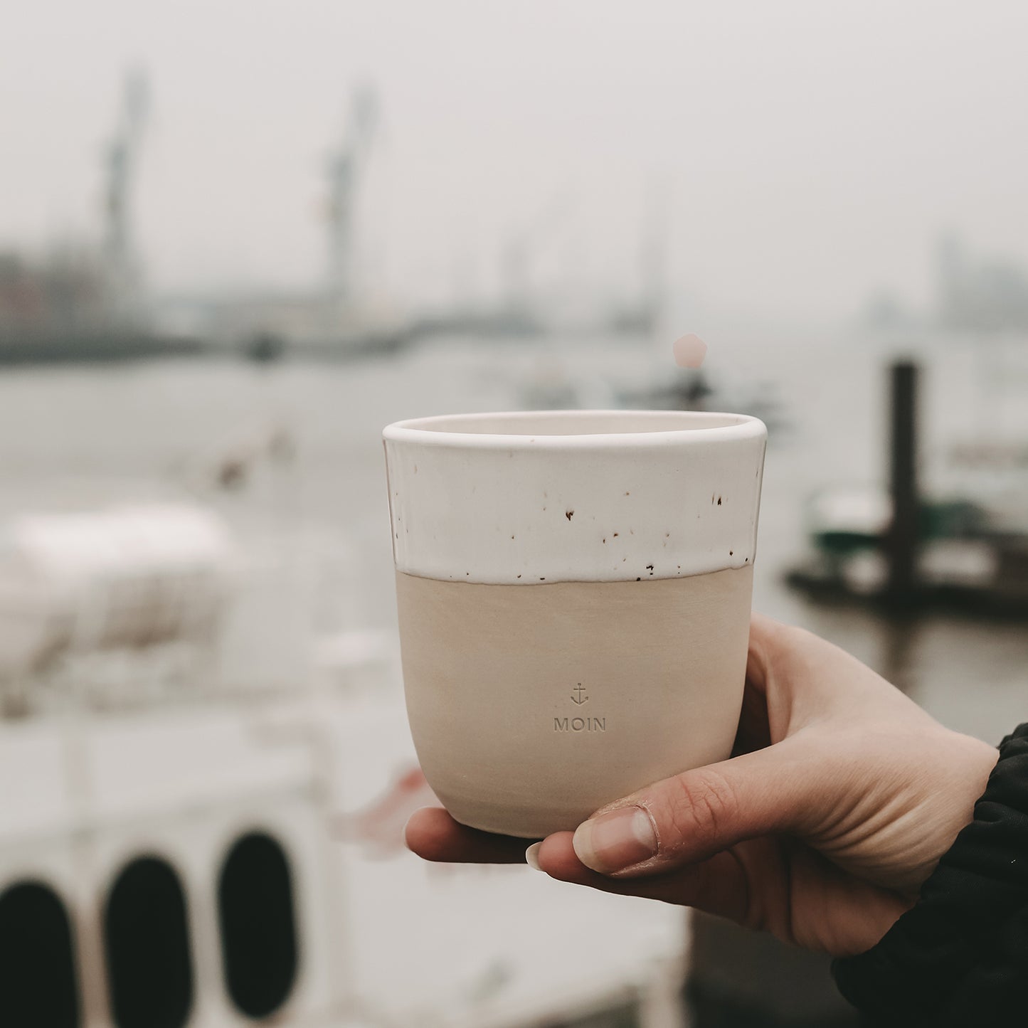 Becher Moin aus Steingut in der Hand gehalten mit Blick auf den Hamburger Hafen